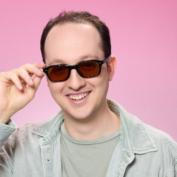 A man smiles and lowers his sunglasses against a pink background. The image relates to the post by visually representing the confident, "deal with it" sentiment behind Hayden Adams announcing Uniswap's protocol fees going live and UNI burns becoming active.
