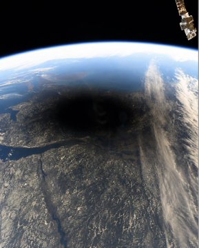 A view from space showing the Earth's surface below and a dark, eclipse-like shadow covering part of the landscape.