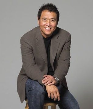 The image shows a smiling man wearing a brown blazer over a black shirt and jeans, sitting on a stool in a posed portrait against a gray background. The accompanying text attributes bold Bitcoin price predictions to Robert Kiyosaki, though the person pictured appears to be a different individual and no verifiable text, names, or identifiers are visible in the image itself to confirm identity.