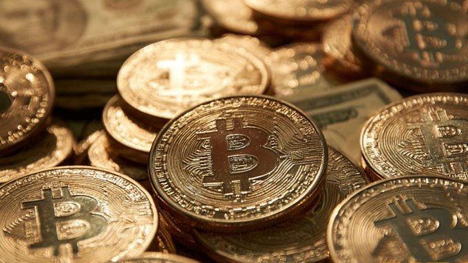 A close-up photograph of multiple physical Bitcoin tokens resting on top of United States dollar bills.