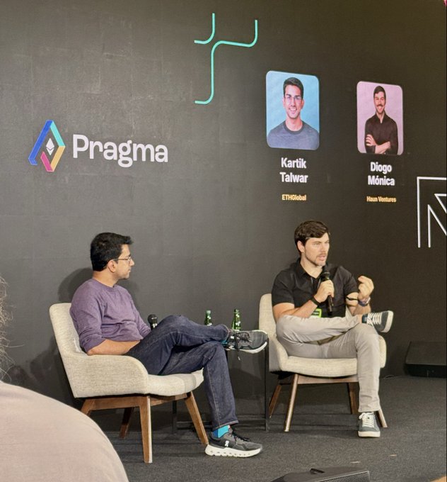 Two men seated in chairs on a stage during a 'Pragma' event, with a backdrop displaying their headshots and names: 'Kartik Talwar' (ETHGlobal) and 'Diogo Mónica' (Meta Ventures).