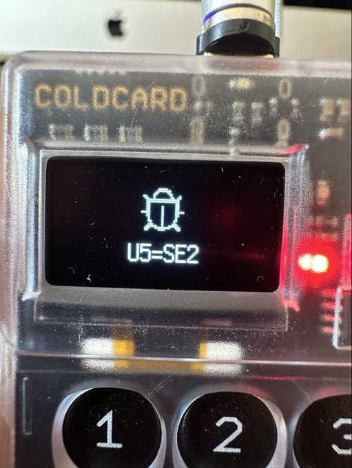A close-up photograph of a Coldcard hardware wallet displaying a lock icon and the text 'U5=SE2' on its screen above the number keys.