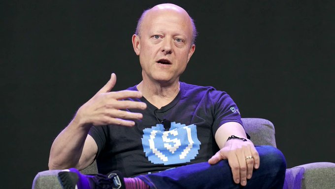 A man in a dark t-shirt gestures while seated on stage, likely discussing the news that Circle, issuer of USDC stablecoin, received final OCC approval to become a federally chartered national trust bank, marking a significant milestone for regulated digital dollars.