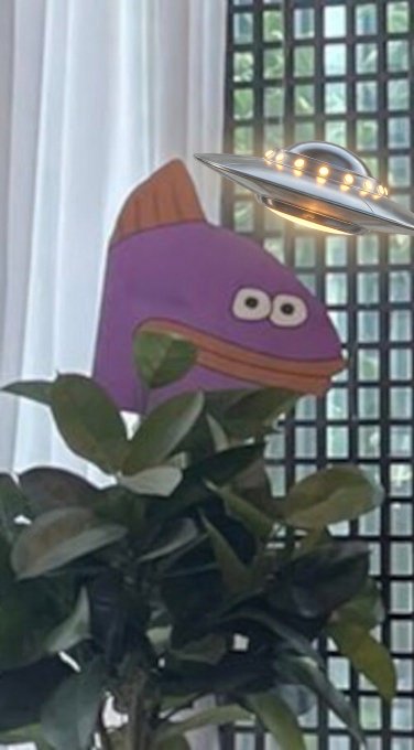 A purple fish cutout decoration placed among houseplant leaves with a decorative UFO light fixture and a window grid in the background.