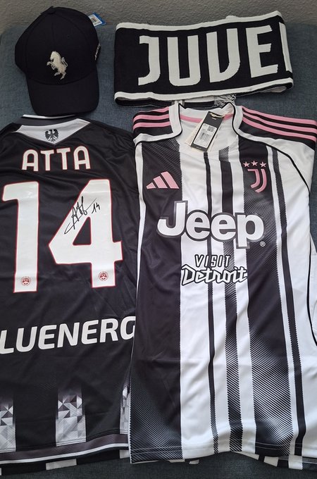 A flat lay displays a black Ferrari cap, a black and white 'JUVE' Juventus scarf, a signed black 'ATTA 14' jersey, and a black and white Juventus 'Jeep' jersey with pink accents.