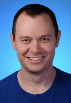 A smiling man with short dark hair, wearing a blue t-shirt, poses against a bright blue background in what appears to be a professional headshot or podcast thumbnail. The image likely represents Benjamin Cowen, the crypto analyst referenced in the post about his admitted wrong prediction on Bitcoin's price.