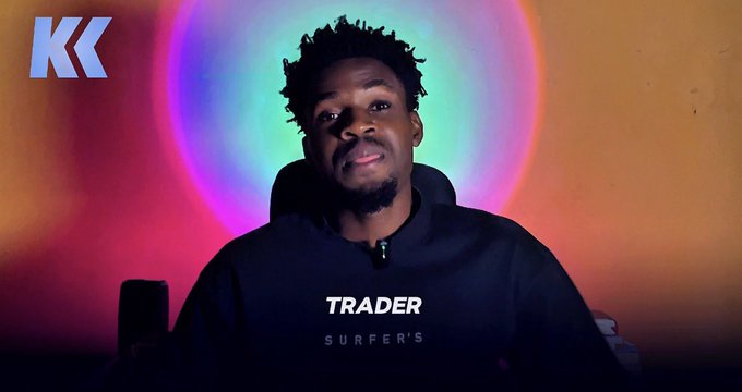A young man in a black hoodie with the word 'TRACKER' visible on it sits against a colorful circular rainbow light backdrop, with a blue 'KK' logo in the upper left corner.