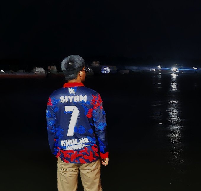 iker, a player for the Khuljars, stands on a beach at night, wearing a blue and red jersey with "Siyam" written in white letters.