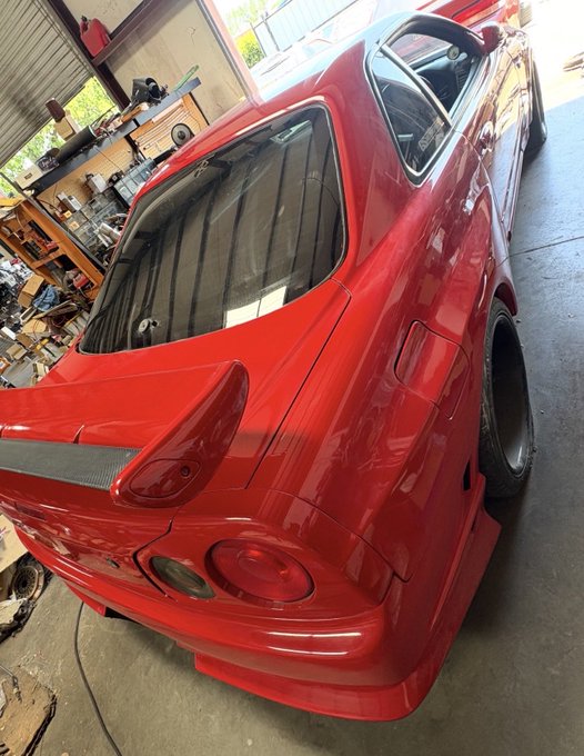 The rear view of a red sports car with a wide-body kit parked in a garage, featuring custom taillights and deep-dish wheels.