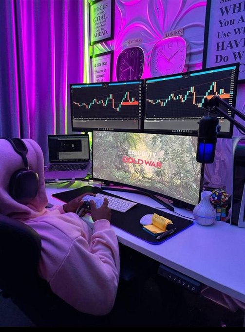 A person in a pink hoodie sits at a gaming setup with multiple monitors displaying trading charts and Call of Duty: Cold War, illuminated by purple neon lighting.