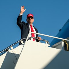 A man in a dark suit and red tie waves while descending the stairs of an aircraft. The red "MAGA" cap suggests this is President Trump, fitting the caption's reference to his comments on Fed rate hikes under Kevin Warsh.