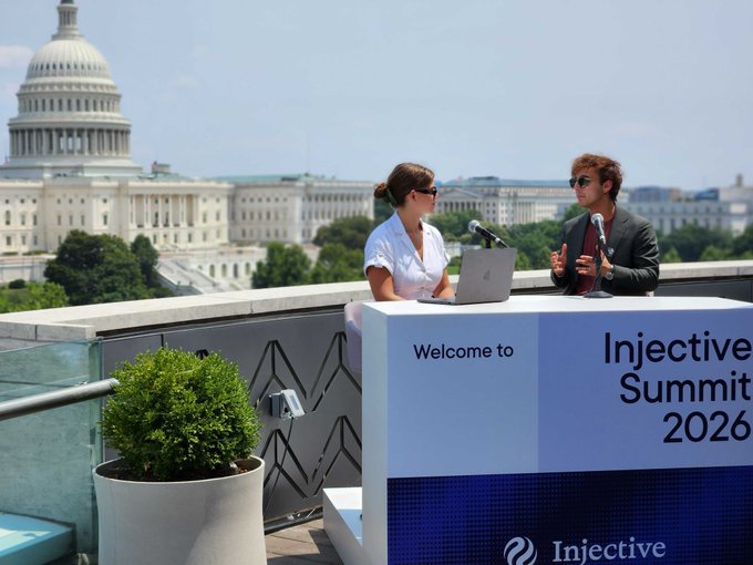 Two hosts sit at a podium labeled "Welcome to Injective Summit 2026" with the Injective logo, broadcasting livestream with the U.S. Capitol building visible in the background, showcasing the Washington D.C. skyline as mentioned in the post.