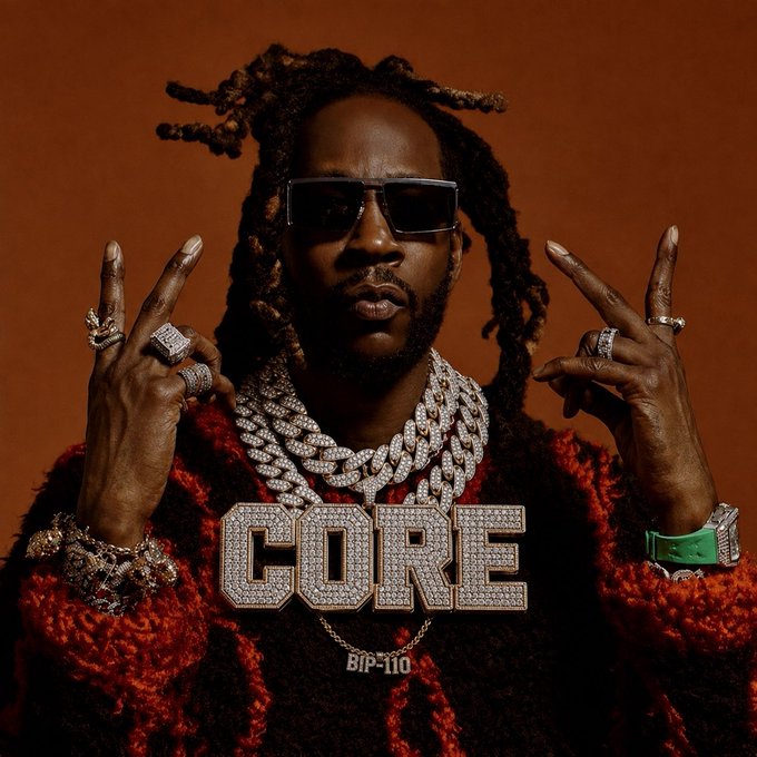 A man wearing sunglasses, multiple diamond chains and rings, and a red furry jacket, with a large diamond 'CORE' pendant and 'BIP-110' necklace.