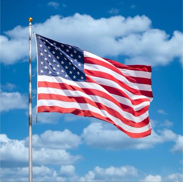 An American flag waving on a pole against a bright blue sky with scattered white clouds.