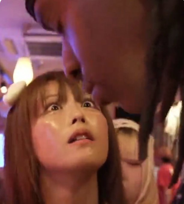 A close-up photo showing a young woman with wide eyes looking up at someone leaning in from above in what appears to be a dimly lit venue.