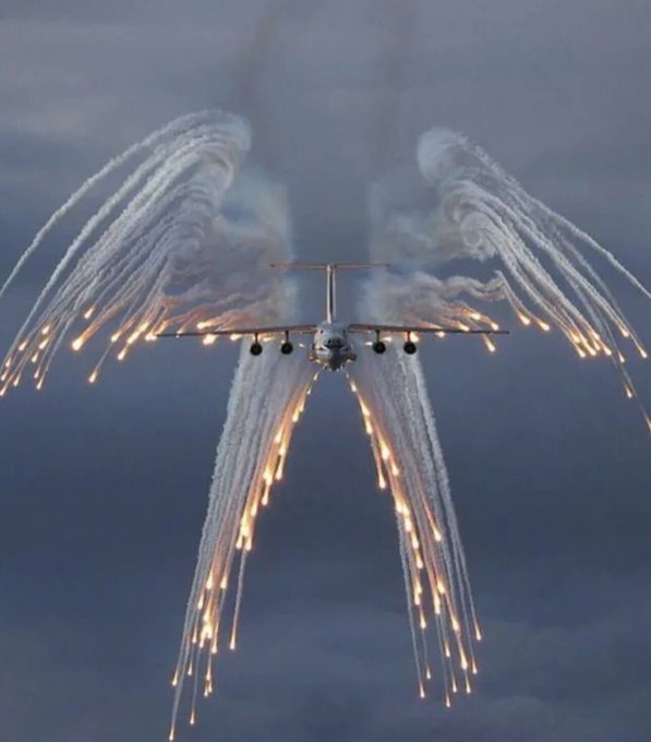 A military aircraft deploys a spectacular array of flares against a cloudy sky, creating a dramatic wing-like pattern as a visual metaphor for the explosive expansion mentioned in the post. The image's dynamic energy and burst of light symbolize the "aero expansion" announcement and the promised live activation on Arc Day one.