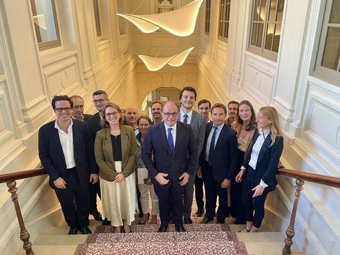 A formal group photograph of approximately a dozen people in business attire standing on a grand staircase beneath a modern chandelier.