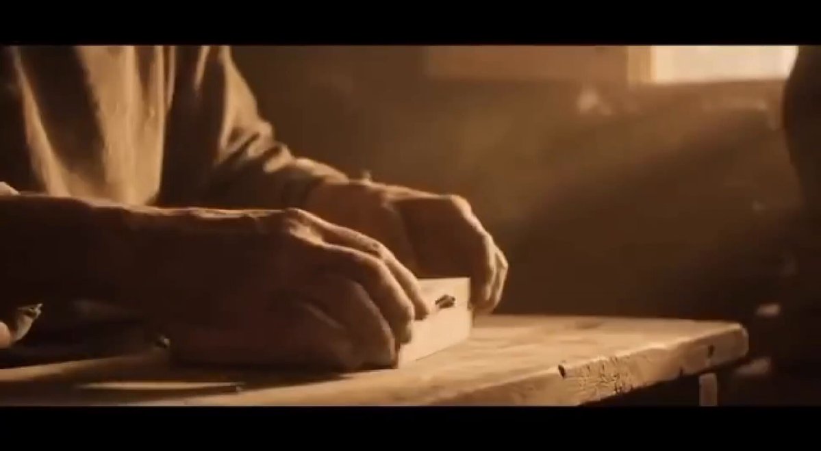 The image shows a close-up of an older man's hands holding a piece of wood, possibly working on a craft project or woodworking task. The background appears to be a dark room with a window that allows natural light into the space. The photo has a grainy texture and is in black and white, giving it a vintage feel. The image also contains text that reads "Not many plays on Solana look like this right now. Clean setup. Unique asset. Bullish momentum building." This text suggests that there might be an interesting story or project behind the scene captured in the photo.