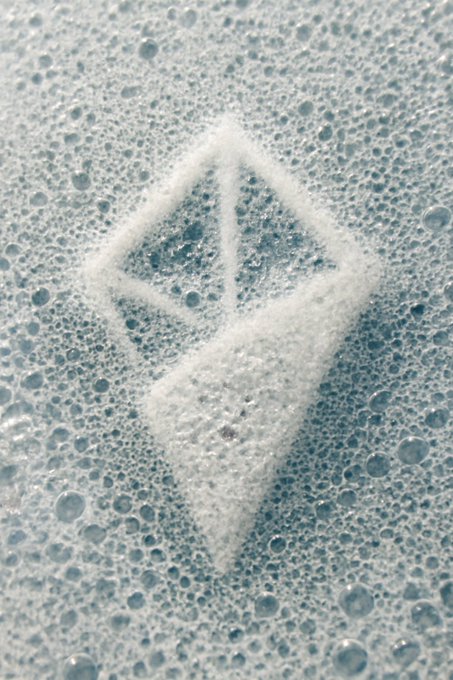 A close-up of soapy water bubbles with a geometric logo shape washed into the foam.
