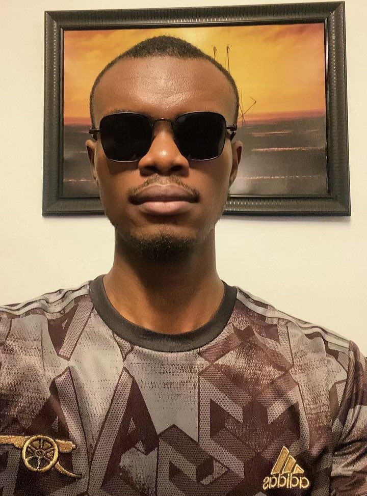 A young man wearing dark sunglasses and an Adidas camouflage-patterned shirt takes a centered selfie in front of a framed sunset painting, projecting a confident expression that complements his observation about his experiences on the "Black app" over the past 72 hours.