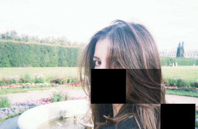 A photograph of a woman with long brown hair in a garden setting, with a black censor box covering the lower half of her face.
