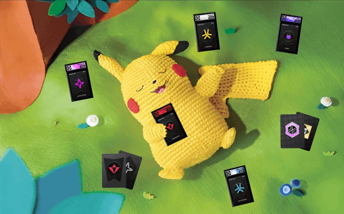 A claymation scene showing a Pikachu figure lying on green grass surrounded by black cryptocurrency-themed cards and small accessories.