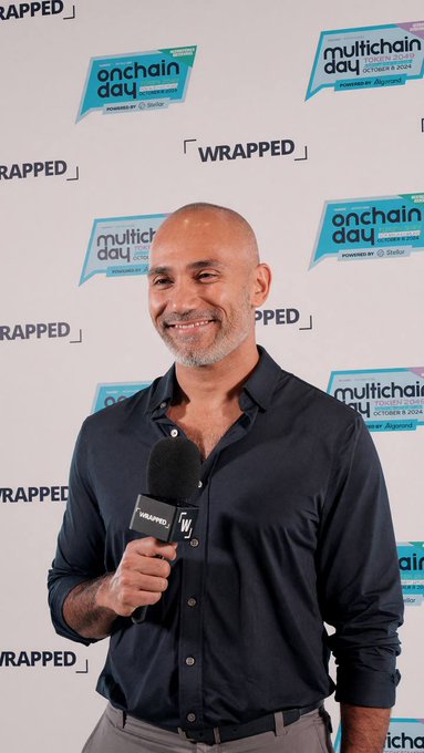 A man with a shaved head smiling while holding a microphone at the 'Multichain Day' event during 'Wrapped' on October 8, 2024.