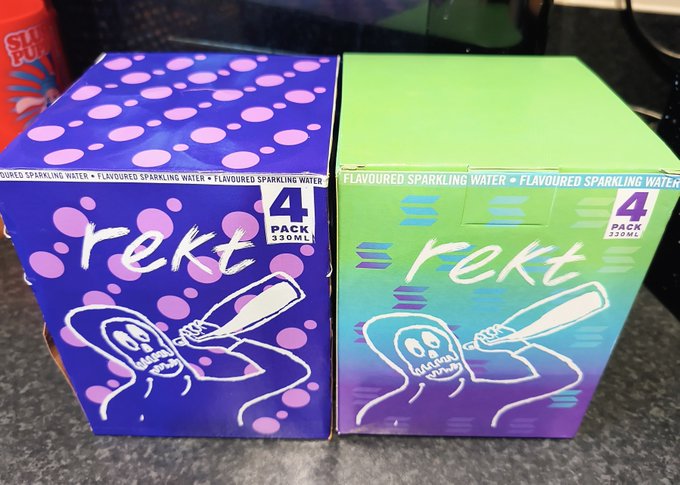 Two 4-pack 330ml boxes of 'rekt' flavoured sparkling water, one purple and one green, sitting on a dark surface.