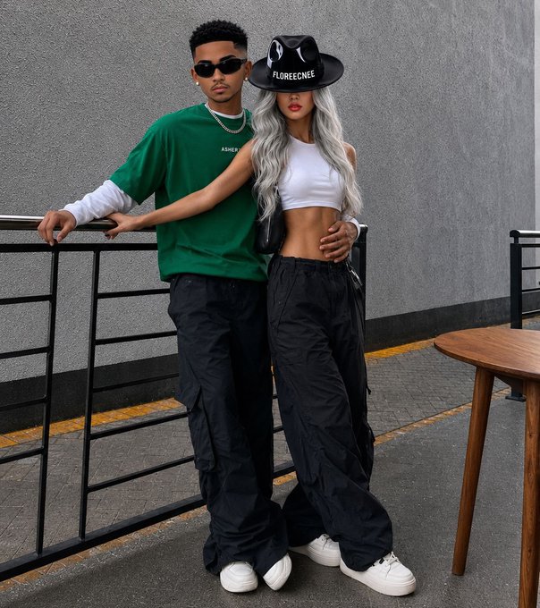 Two young people posing together on a street; one wears a green shirt and sunglasses, the other wears a white crop top, black cargo pants, and a black cowboy hat labeled 'FLORECEENEE'.