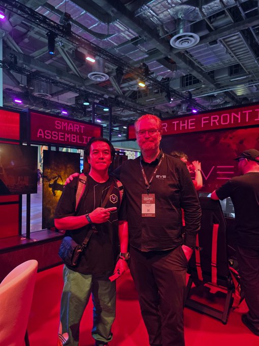 Two people pose for a photo at a convention, standing in front of an EVGA booth with banners reading "SMART ASSEMBLY" and "OVER THE FRONTIER" visible behind them.