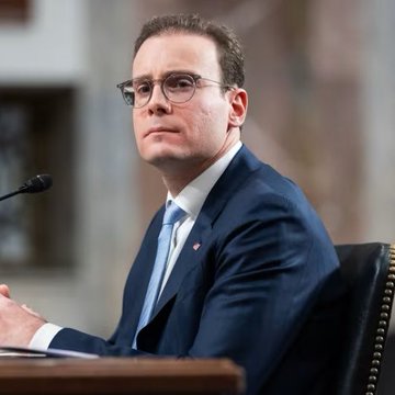 A man in a dark suit and glasses speaking at what appears to be a Senate hearing, with a microphone in front of him.