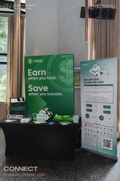 USDD crypto promotional booth display with green signage reading 'Earn when you hold. Save when you transfer' alongside a 'Bank with USDD' information panel.
