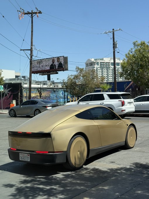 A sleek gold Tesla Cybertruck is parked on a city street, with a "Catle House" billboard visible in the background — a futuristic sight that easily warrants a "Woah."