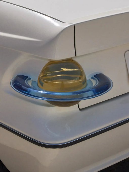 Close-up of a modern white bathroom fixture featuring a translucent amber/orange globe-shaped drain or stopper held in a clear blue plastic holder.