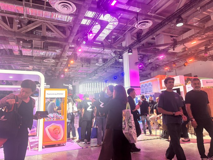 Attendees gather at a tech conference with purple lighting, near booths including one labeled 'Payments by PPRO'.
