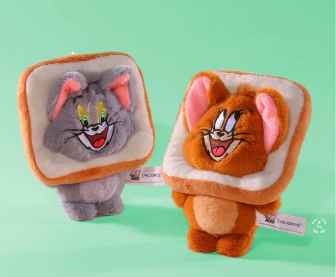 Two plush toys designed as Jerry and Tom from Tom and Jerry, with their faces printed on slices of bread that they carry on their backs, branded with 'MUGKIS' tags.
