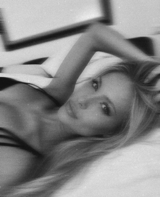 A black and white photo of a woman with long blonde hair lying down, resting her arm above her head.
