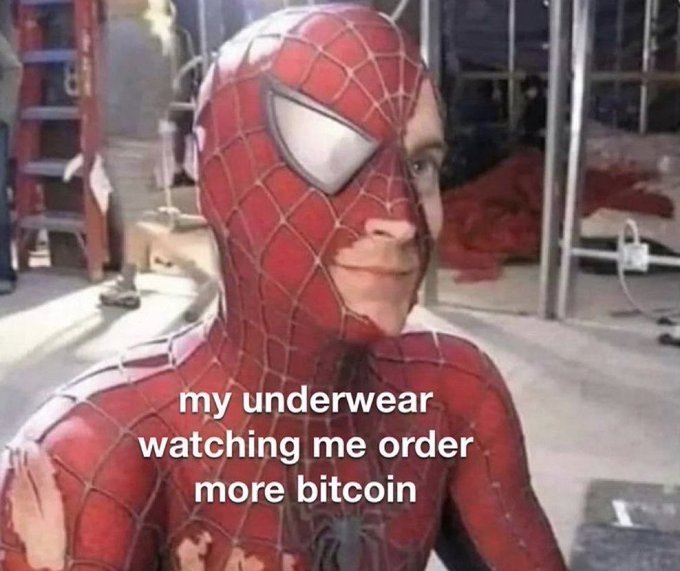 A behind-the-scenes photo of Tobey Maguire in the Spider-Man suit, with the mask pulled back to reveal his face, overlaid with the text "my underwear watching me order more bitcoin".