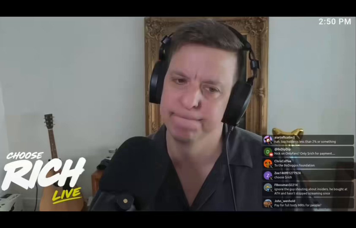 The image shows a man wearing headphones, sitting behind a microphone while talking about his radio show. The background features a white wall with a gold frame hanging above it. There are also two guitars visible in the scene - one near the left side of the room and another on the right side.