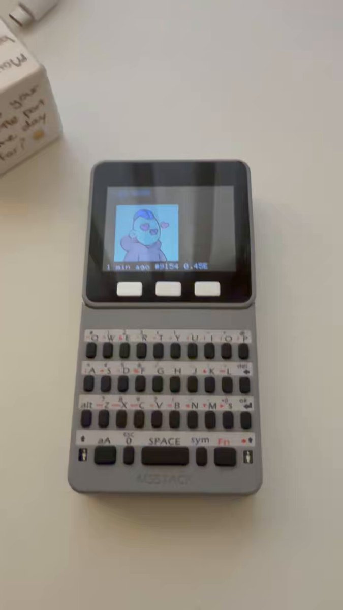 The image features a small, gray electronic device with a screen that displays a cartoon character. The device appears to be a keyboard or a computer mouse, possibly used for browsing the internet or playing games. In the background of the image, there is a white box containing a message written in black text.