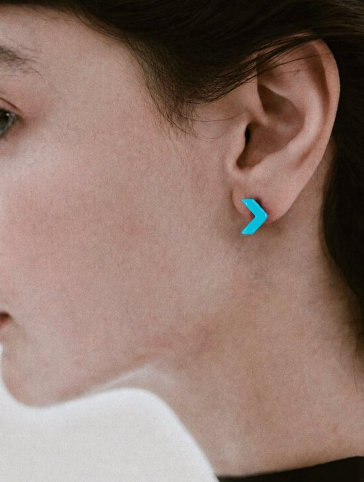 A close-up of a person's ear wearing a small turquoise chevron/arrow-shaped earring, complementing the post's Chinese text "是时候来点耳目一新的东西啦！" which translates to "It's time for something refreshing to see and hear!" The bright blue geometric earring serves as a fresh, eye-catching accessory that matches the message about bringing something new and exciting.
