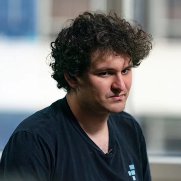 A young man with curly hair wearing a black t-shirt, looking off to the side.