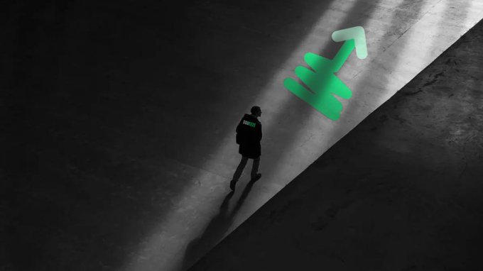 An overhead shot of a solitary figure standing in a beam of light, with a large green dollar sign cast as a shadow or projection on the ground.