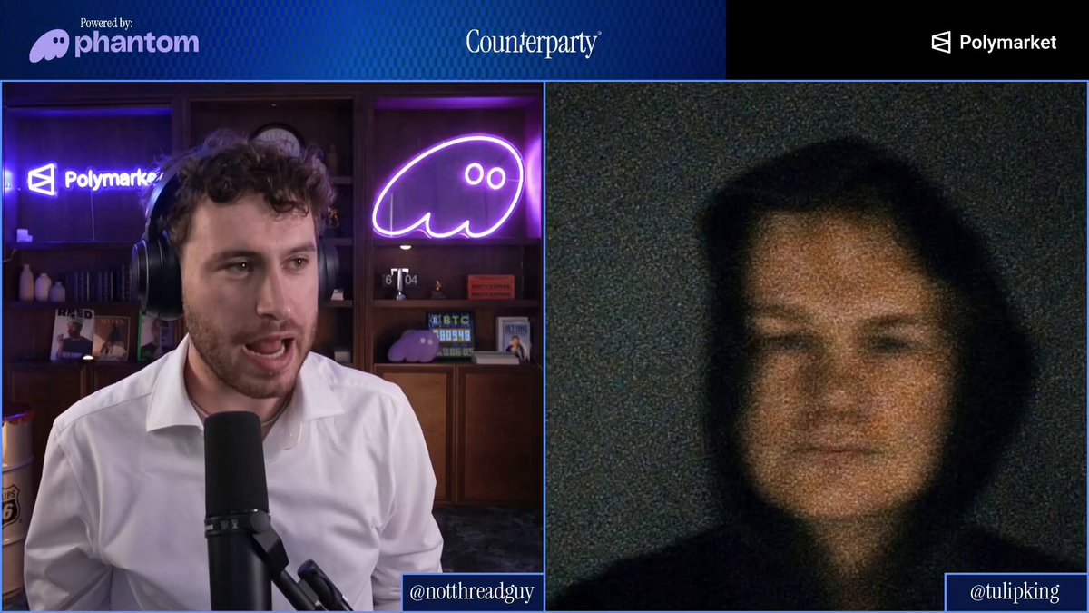 The image shows two men talking into microphones, with one man wearing headphones and the other speaking directly into the microphone. The background features a blue wall with a neon sign that reads "Conversation Party" and another sign that says "Polymark". There is also an image of a person's face on the screen behind them.