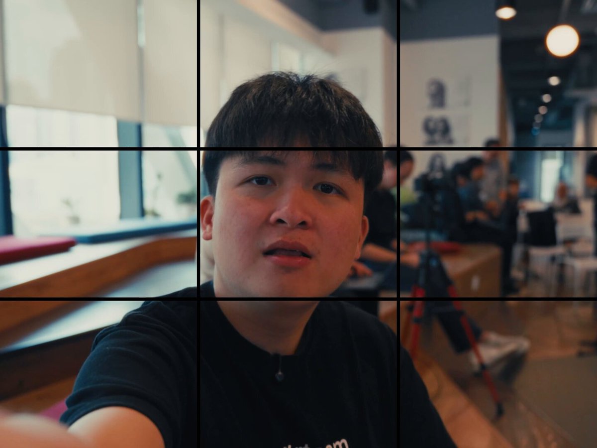 The image features a young man wearing a black shirt, sitting at a table with his hand outstretched towards the camera. The photo has been edited into multiple sections or squares, which are arranged vertically against a gray background. This composition creates an interesting visual effect that draws attention to the subject and adds depth to the image.