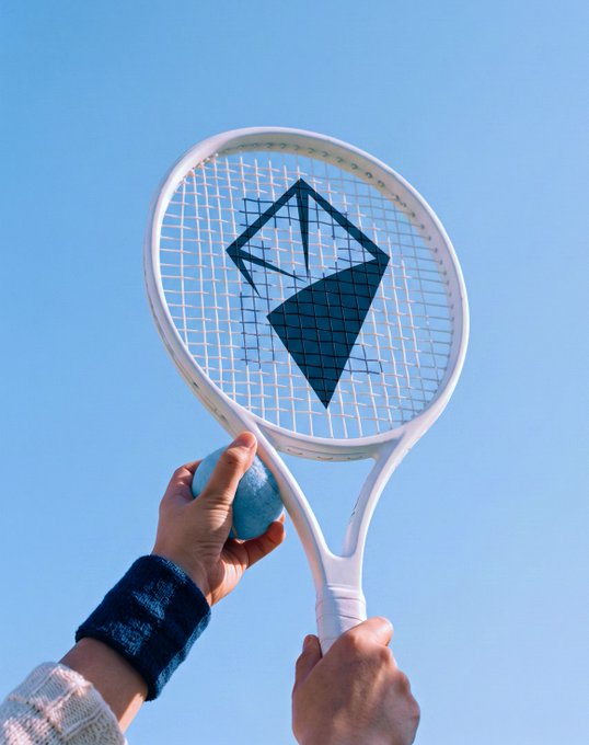 A hand holds a white tennis racket featuring a dark blue geometric logo, with a small blue ball gripped alongside the handle, set against a clear blue sky. The image's tennis gear symbolizes the post's theme of focus, precision, and "making it count" in the fast-moving crypto and AI space.