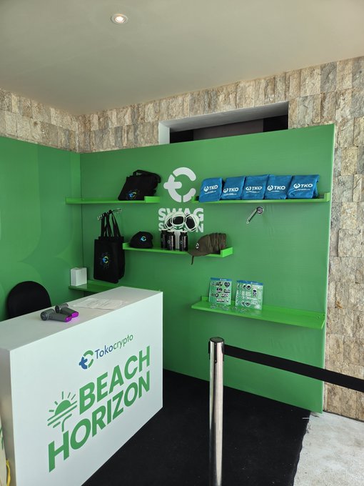 A promotional booth displays 'Tokocrypto' and 'BEACH HORIZON' branding with green walls, shelves of merchandise including 'TKO' branded bags and sunglasses.