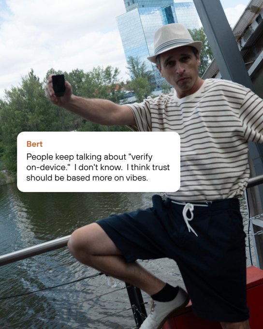 A man in a striped shirt, shorts, and straw hat posing with one leg up on a railing by a body of water, holding a small black device, with an overlaid message from 'Bert' reading 'People keep talking about "verify on-device." I don't know. I think trust should be based more on vibes.'