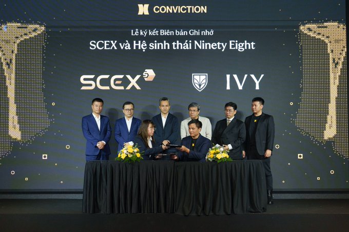 A signing ceremony at a CONVICTION event where SCEX and the Ninety Eight ecosystem (IVY) sign a memorandum of understanding, with executives and representatives standing behind a black-draped table on stage.