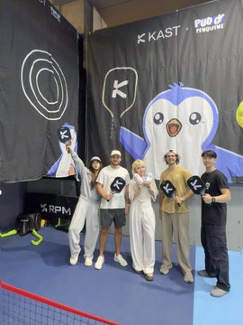 Five young people posing together at what appears to be a KAST x Pudgy Penguins promotional event, with one person in a penguin mascot costume, in front of branded backdrops featuring the KAST, Pudgy Penguins, and RPM logos.